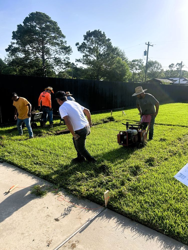 Construction workers on a green lawn using machines and working near a fence.