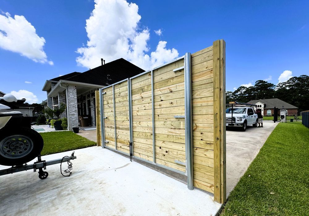 Wooden gate with metal supports on a driveway in front of a house. A truck is parked nearby.