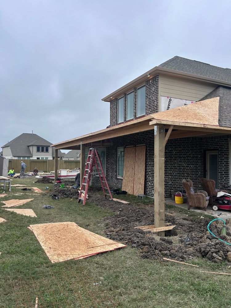 Construction of a covered patio attached to a brick house with a brown roof.
