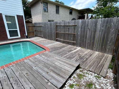 Wooden deck surrounding a pool, with a gray wooden fence in the background.