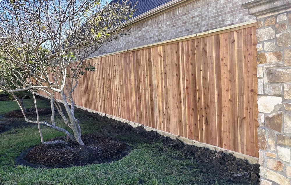 Wooden fence alongside a house with a tree in the foreground, and stone column on the right.