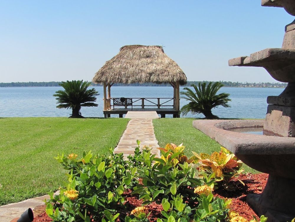 Gazebo with thatched roof on a lake, pathway through green lawn.