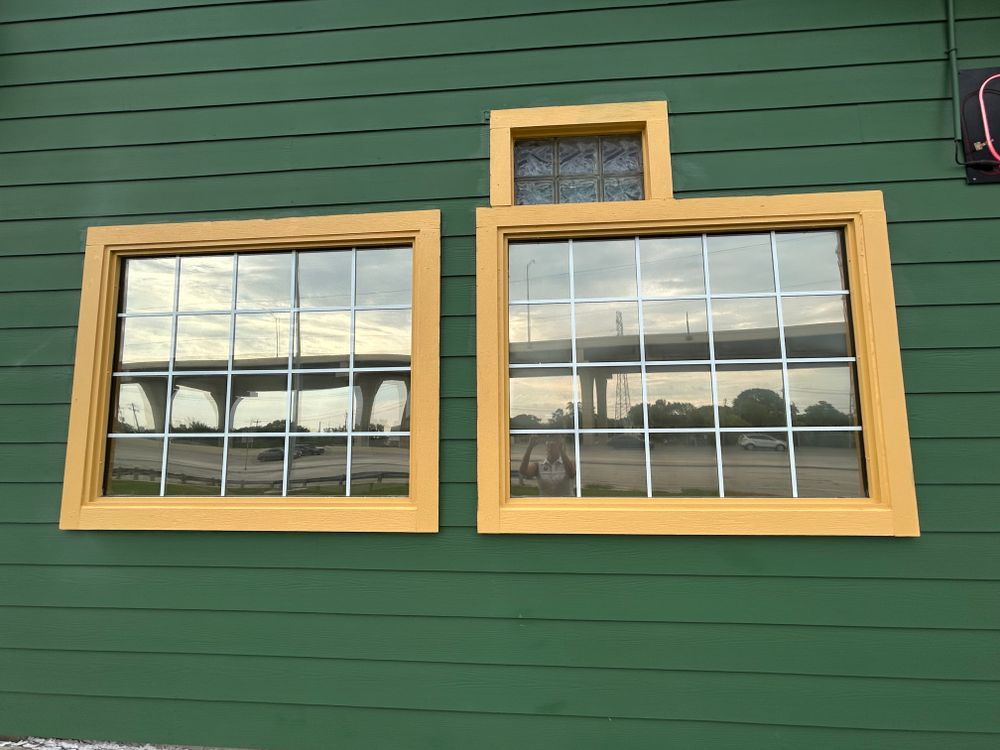 Green building with yellow-framed windows reflecting a bridge and sky; small square window above.