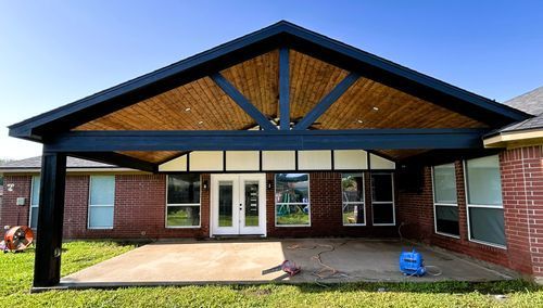 Covered patio with black beams, wood ceiling, brick house, and concrete patio.