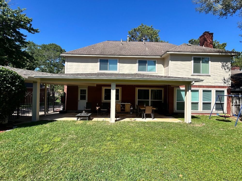 Rear view of two-story house with covered patio, brick, red accents, and green lawn.