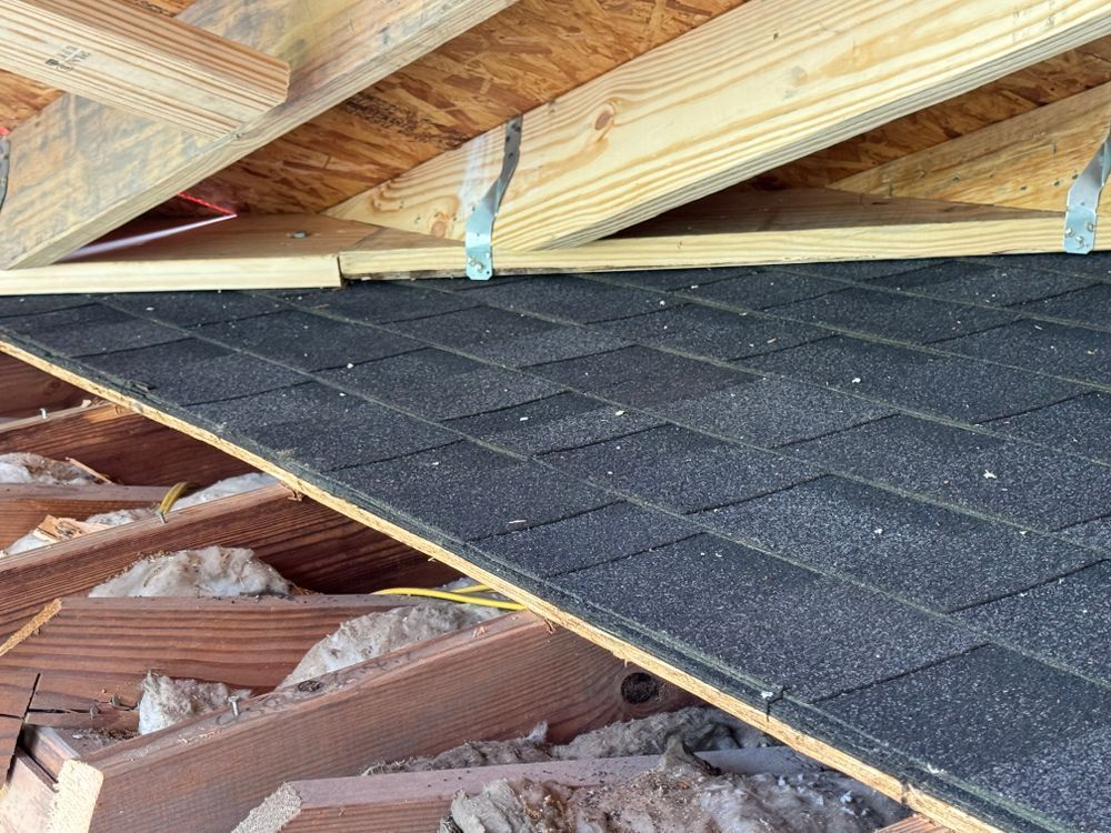 Partially constructed roof with dark shingles, wooden beams, and insulation.