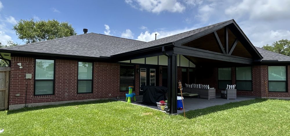 A brick house with a covered patio, green lawn, and blue sky.