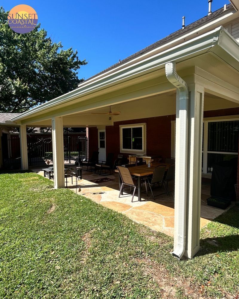 Covered patio with beige pillars, a red house, outdoor furniture, and green grass.