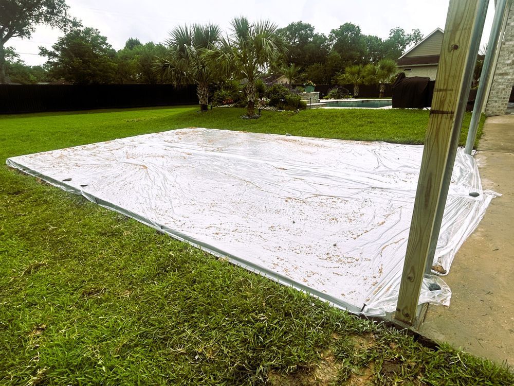 A white tarp covers a rectangular area of green grass, with a pool and house in the background.