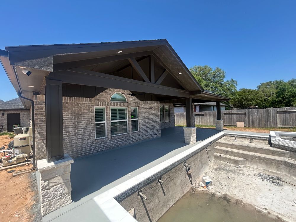 Covered patio with dark beams and brick. Overlooks a pool under construction.