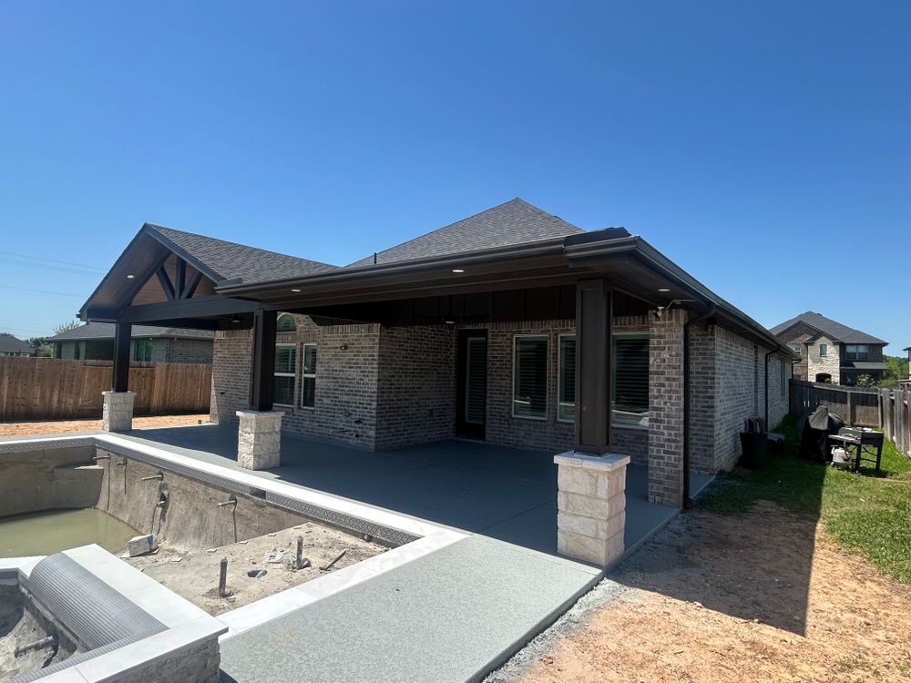 Backyard patio with brick home and pool under construction. Overhang and columns.