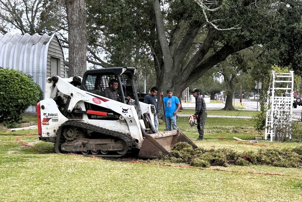 Bobcat removing debris from a yard, several men watch.
