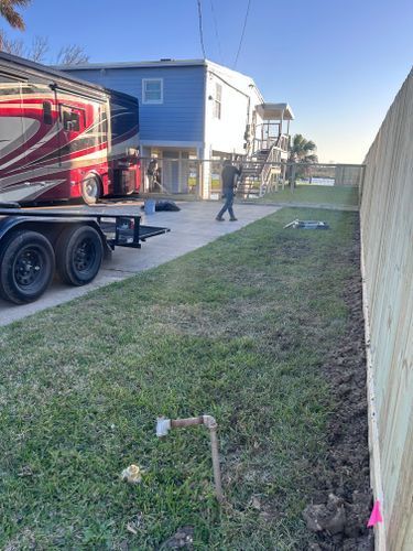 A person walks past a blue house and RV parked on a driveway next to a newly built wooden fence.