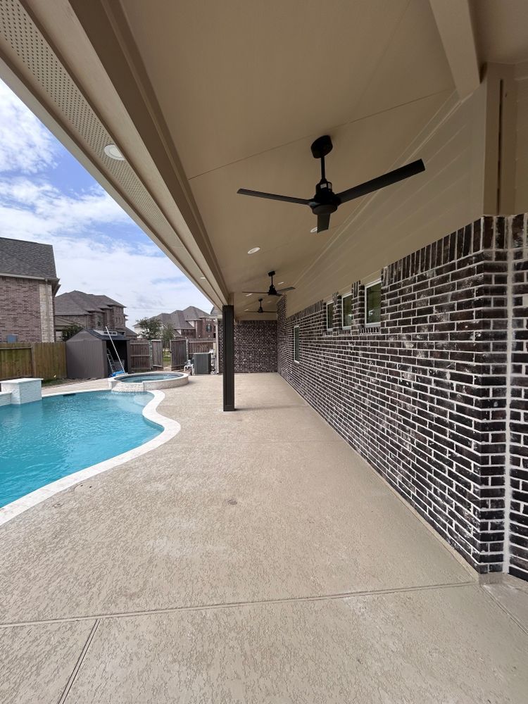 Covered patio with a pool, brick wall, ceiling fans, and concrete flooring.