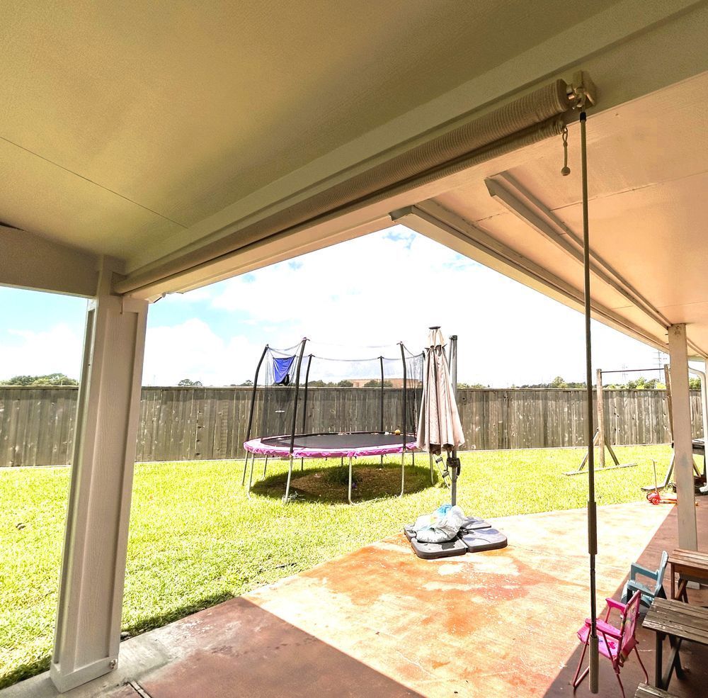 Covered patio overlooking a backyard with a trampoline and umbrella on a sunny day.