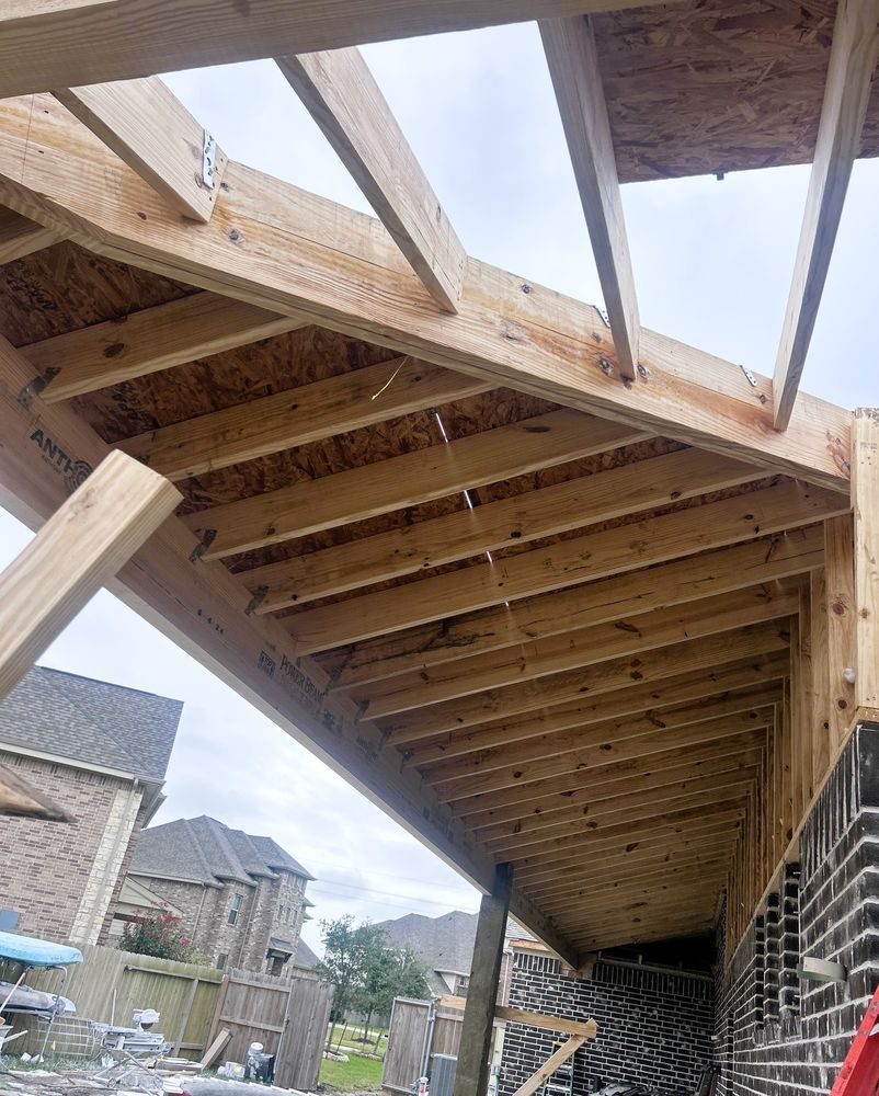 Wooden framework of an angled roof under construction, attached to a brick wall.