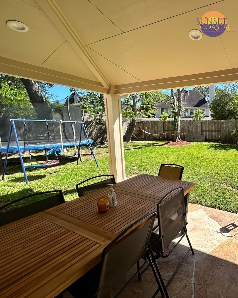 Covered patio with wooden table and chairs overlooking a backyard with trampoline and trees.