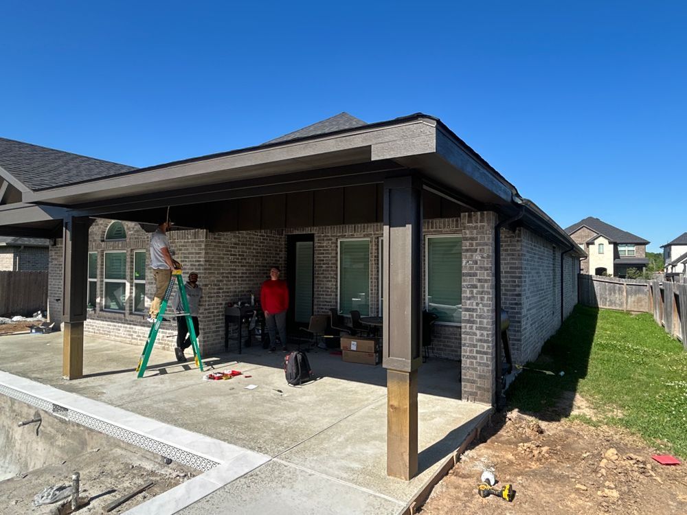 Construction of a patio cover on a brick house; workers, tools, concrete patio, sunny day.