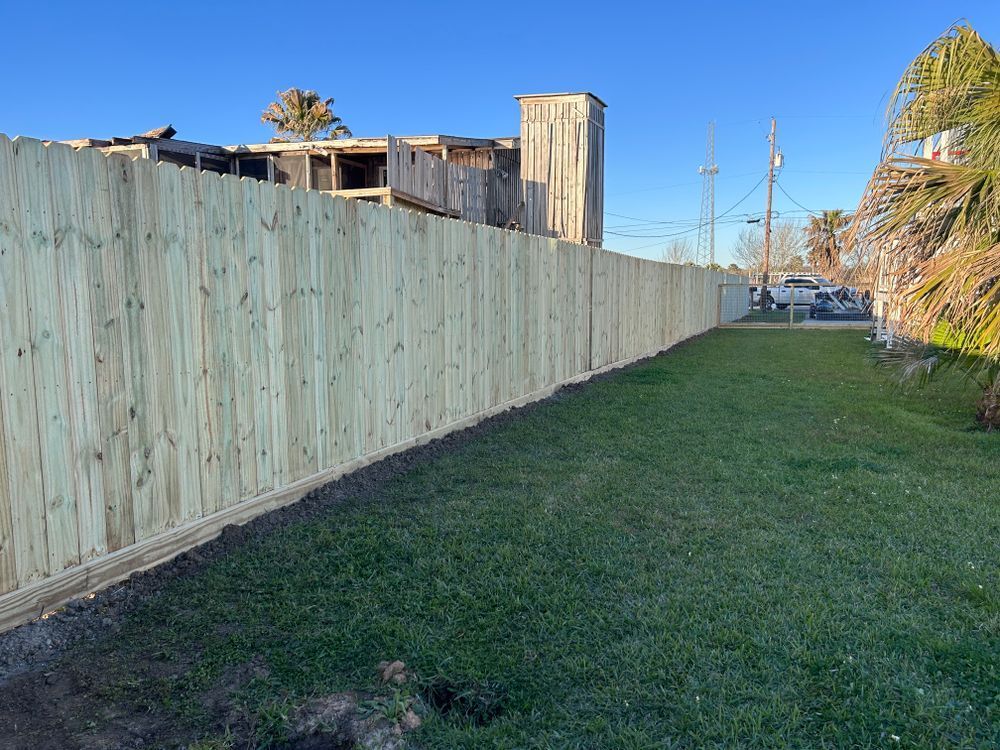 Wooden fence along a grassy area with a building in the background on a sunny day.