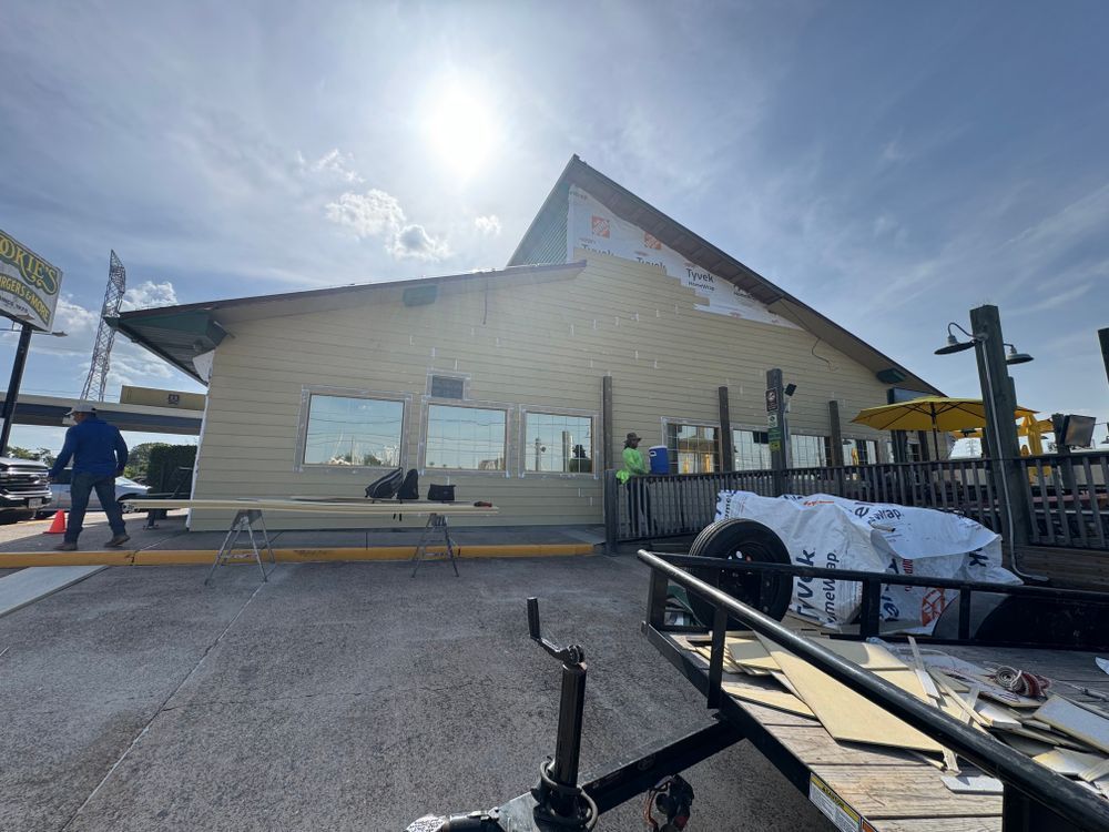 Construction on a tan building with a triangular roof, sunny day, workers present.