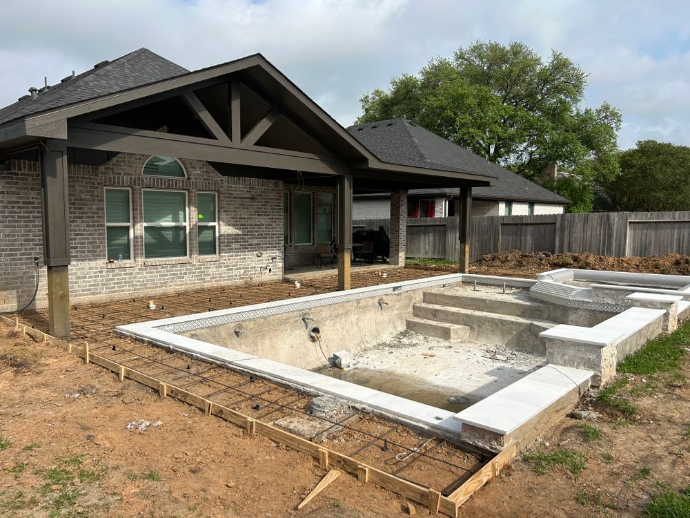 Pool under construction next to a brick house with a covered patio, outdoor setting.