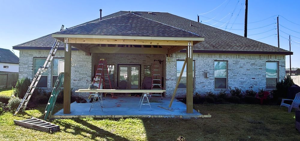 Construction in progress: building a covered patio on a house with brick siding and a dark roof.