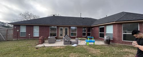 A red brick house with a dark roof and a concrete patio, a person standing, cloudy day.
