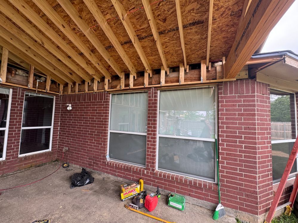Brick house exterior with wooden roof framing over windows during construction.