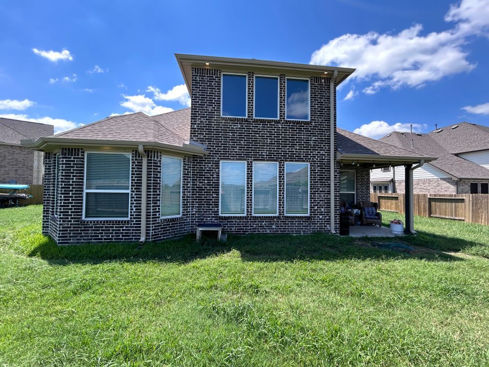 Back of a house with dark brick siding, windows, and a covered patio on a sunny day.