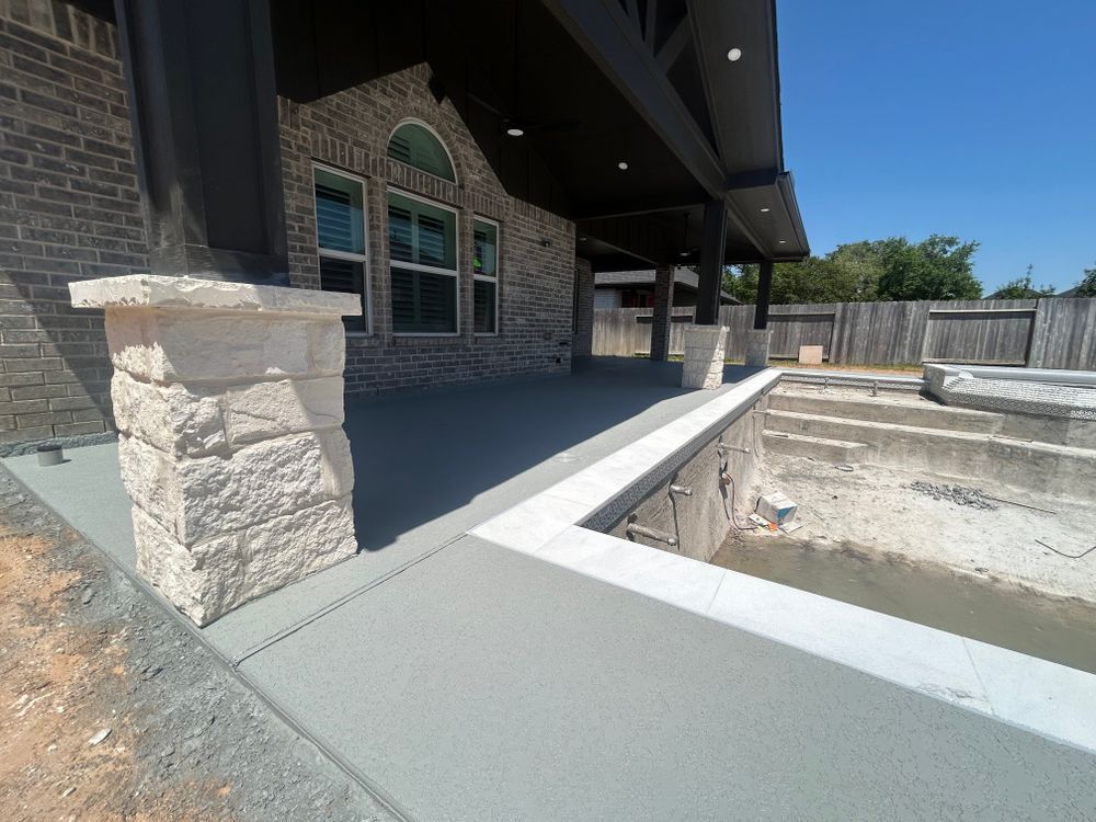 Exterior view of a house with a gray patio, pool, and stone columns on a sunny day.