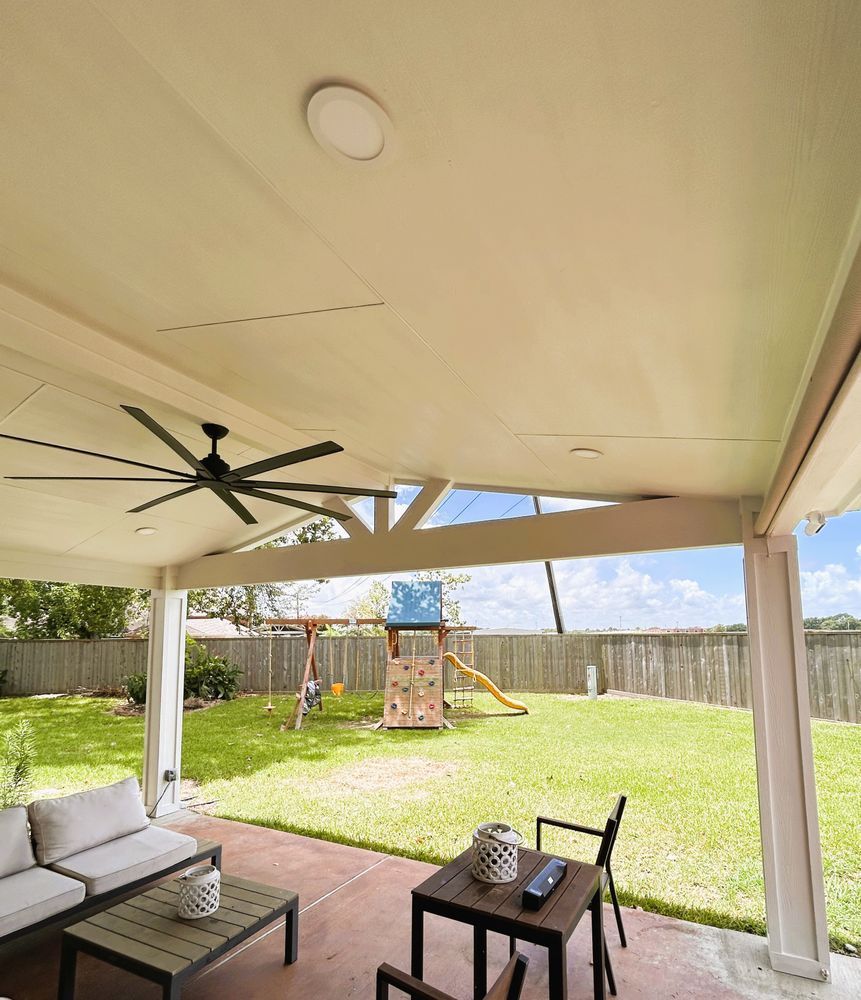 Covered patio with seating, ceiling fan, overlooking a backyard with a playset.
