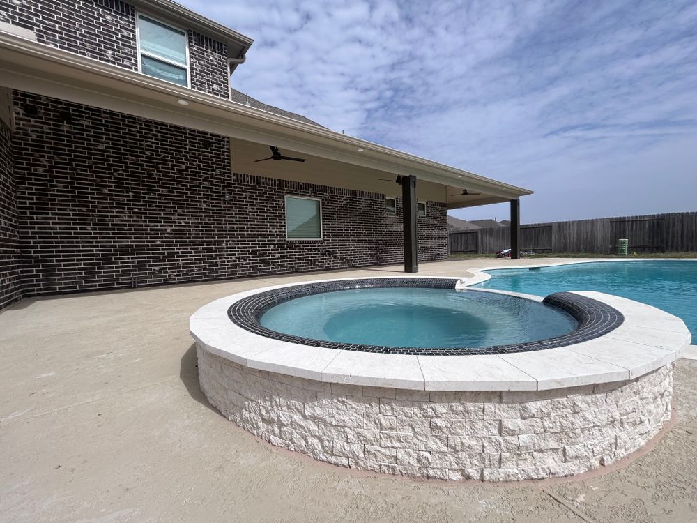 A backyard with a hot tub, pool, and covered patio. Brick house exterior, blue sky.