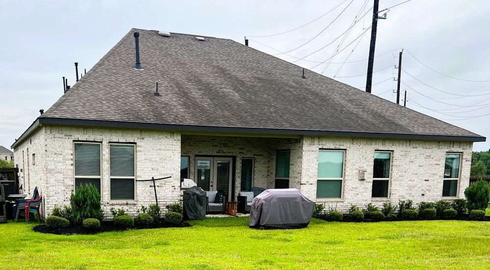 Back of a brick house with a gray roof, windows, and a grassy yard.