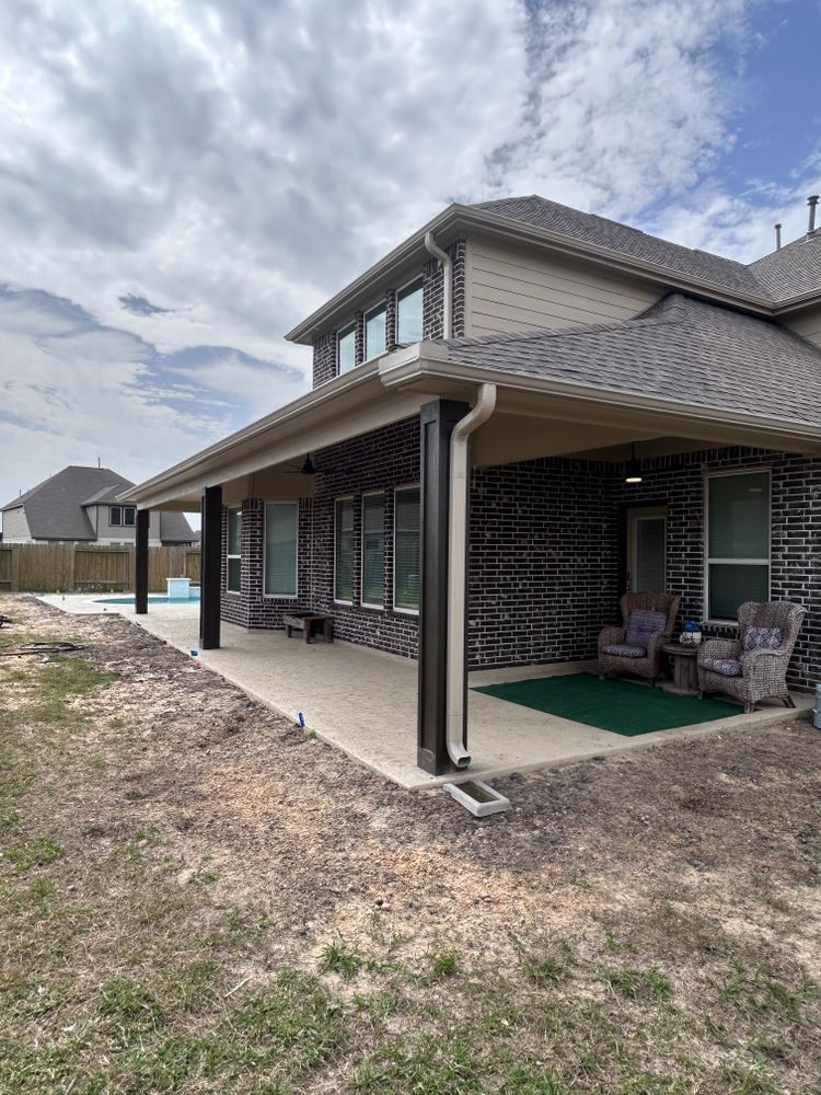 A covered outdoor patio with dark columns, brick walls, and comfortable seating; backyard setting.