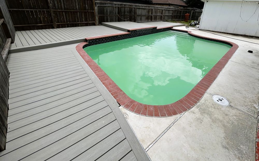 Backyard pool with green water, surrounded by brick, concrete, and a gray wooden deck.