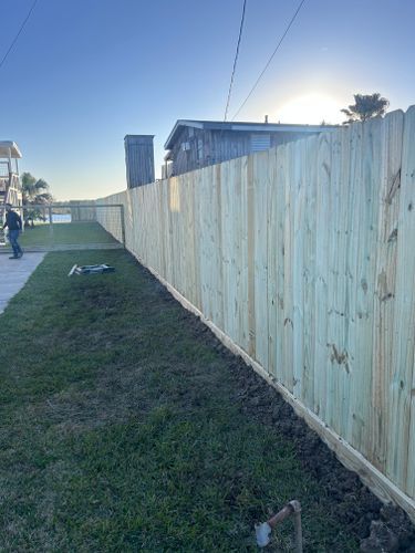 A new wooden fence along a grassy lawn; person stands beside it. Sunlight shines.