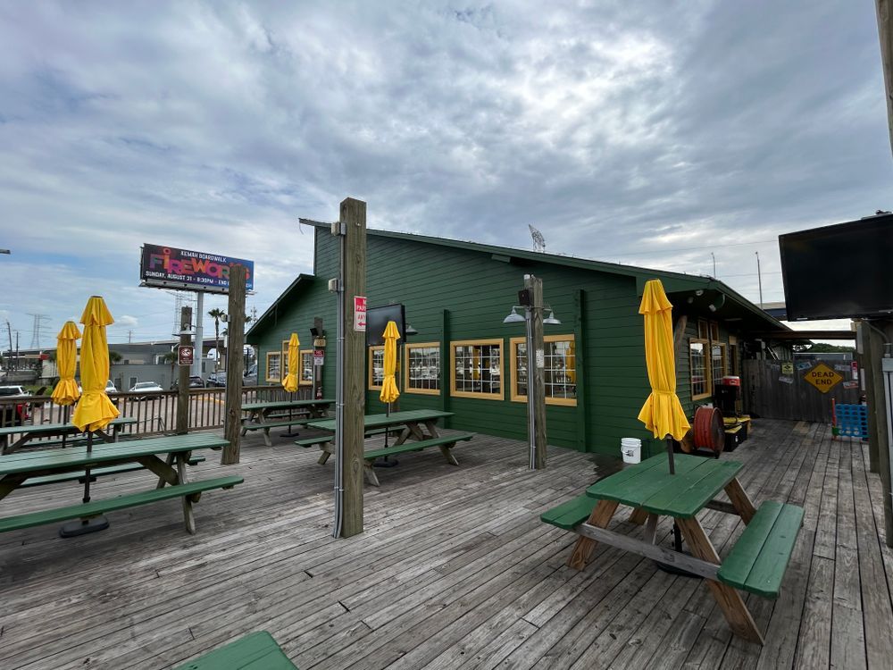 Green outdoor restaurant with picnic tables and yellow umbrellas, cloudy sky.