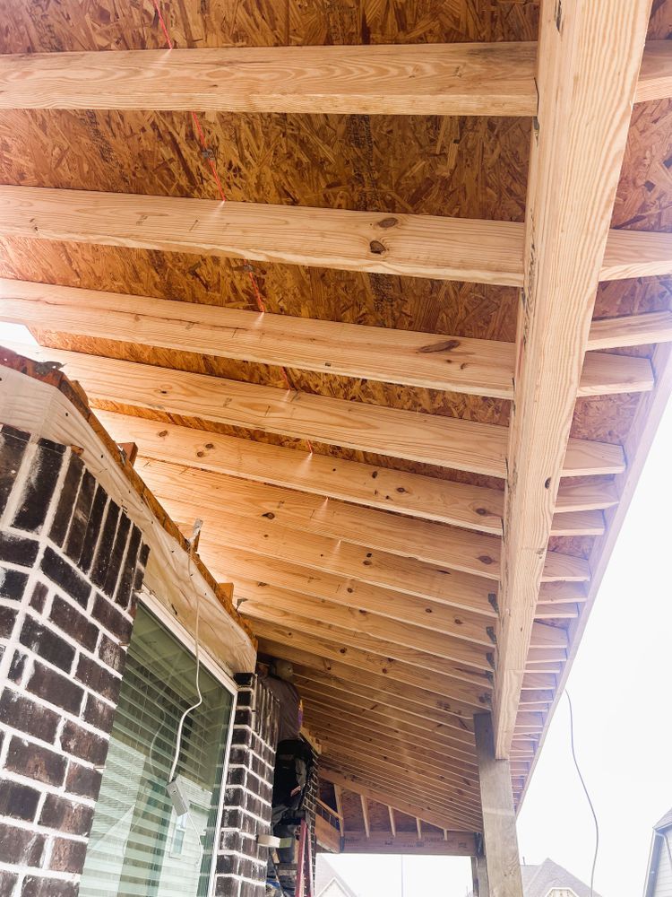 Under-construction wooden roof of a porch with brick wall on the left.