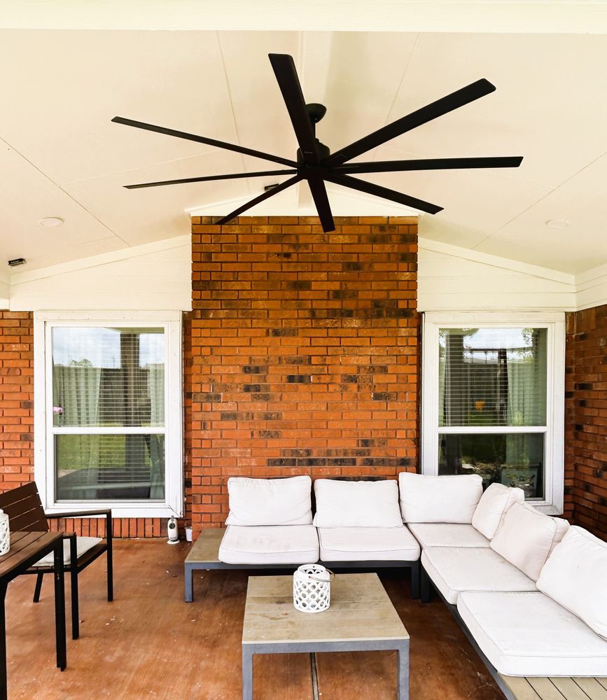 Outdoor patio with sectional seating, brick wall, large black ceiling fan.