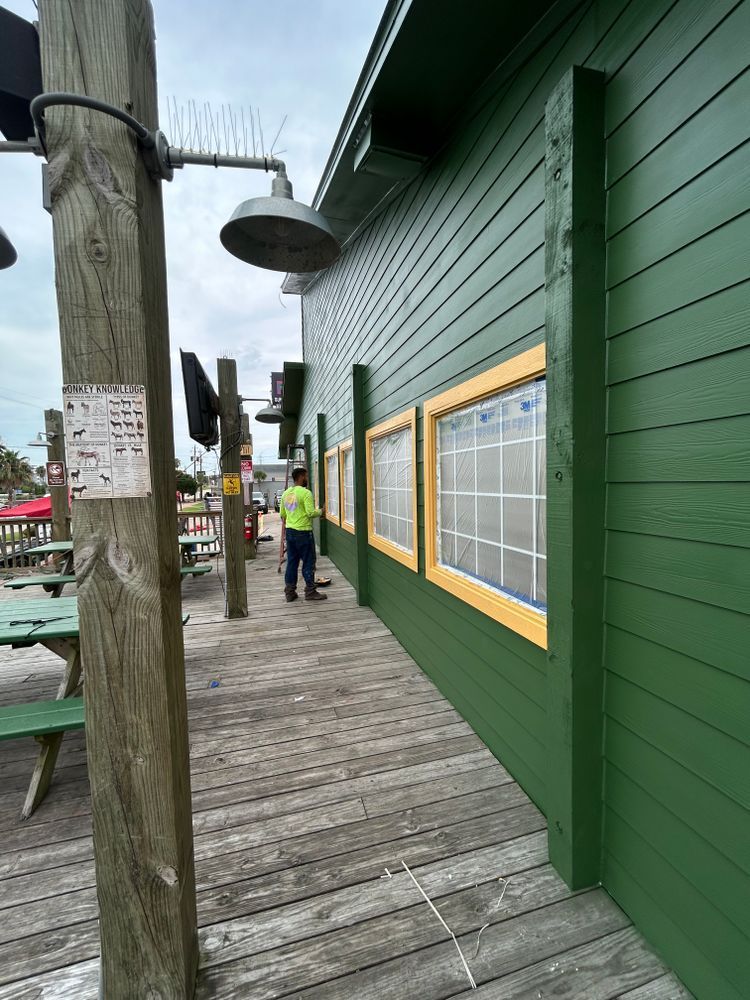 Wooden deck and green building with yellow-framed windows. A person in neon green works nearby.