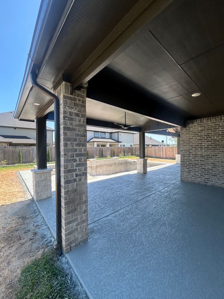 Covered patio with brick columns and concrete floor, looking toward a backyard.