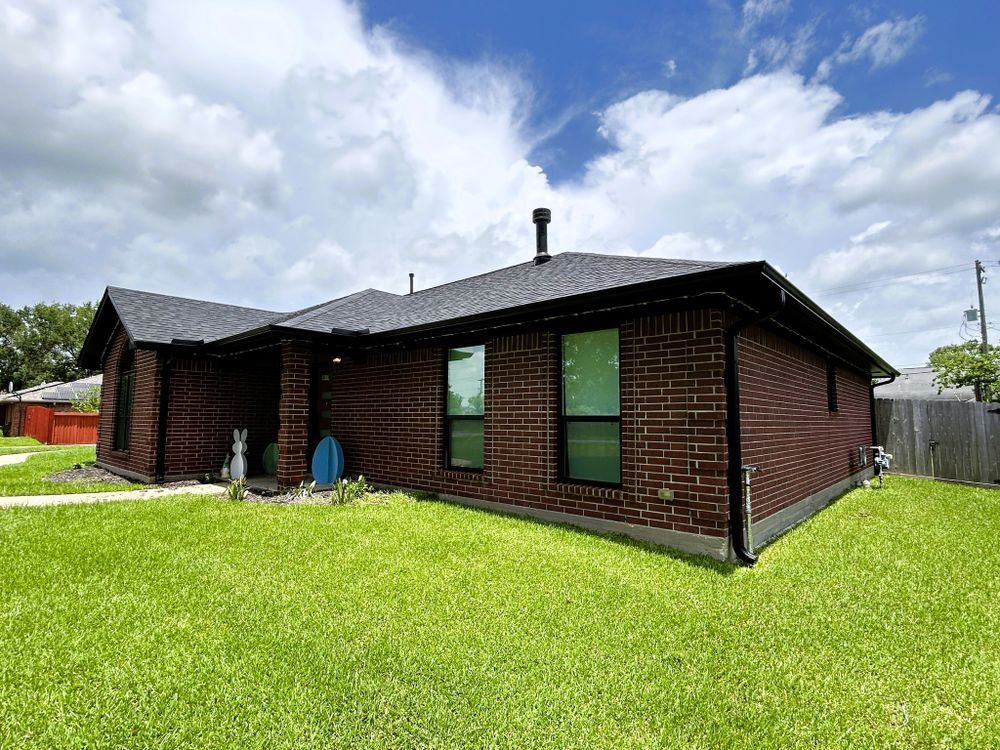 Red brick house with green lawn and cloudy sky.