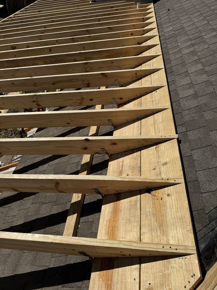 Wooden roof under construction; rafters on plywood; dark shingles visible.