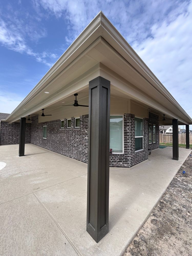 Covered patio with dark columns, brick wall, and concrete floor under blue sky.