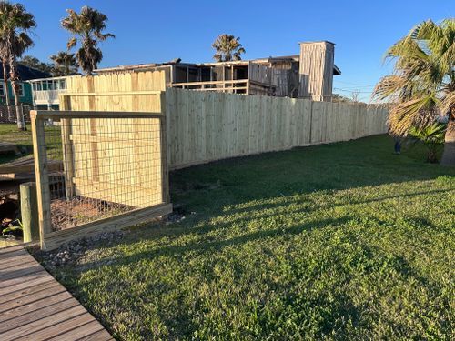 Wooden fence bordering a grassy yard next to a dock and building with palm trees.