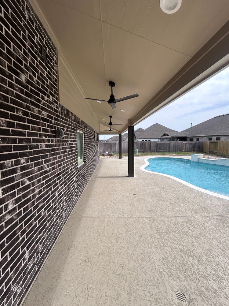 Covered patio with brick wall, ceiling fans, concrete floor, and pool in the background.