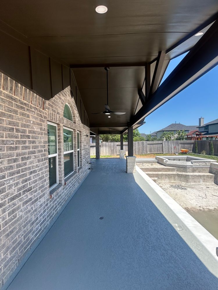 Exterior covered patio with gray flooring, brick wall, and a view of a backyard pool.