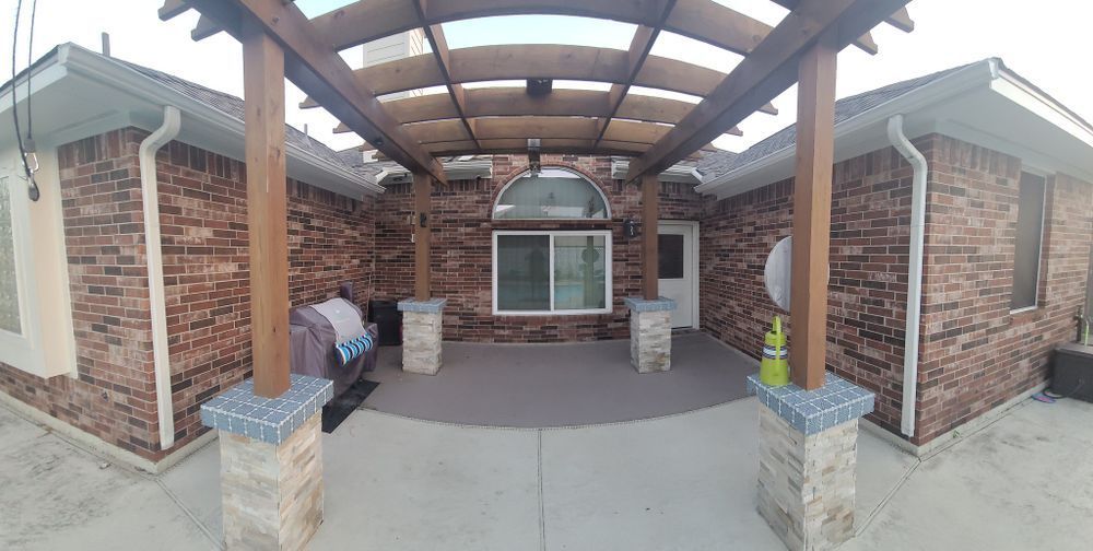 Back patio with brick walls, a wooden pergola, and a gray concrete floor.