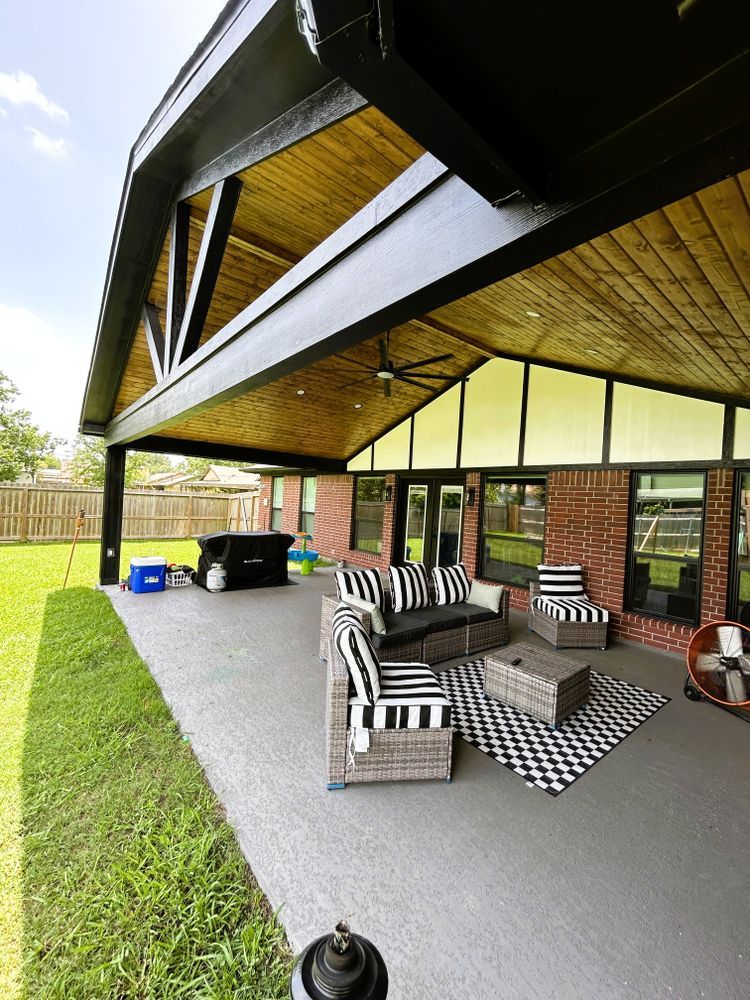 Patio with seating, a grill, and a wooden ceiling. Black and white striped cushions. Brick wall.