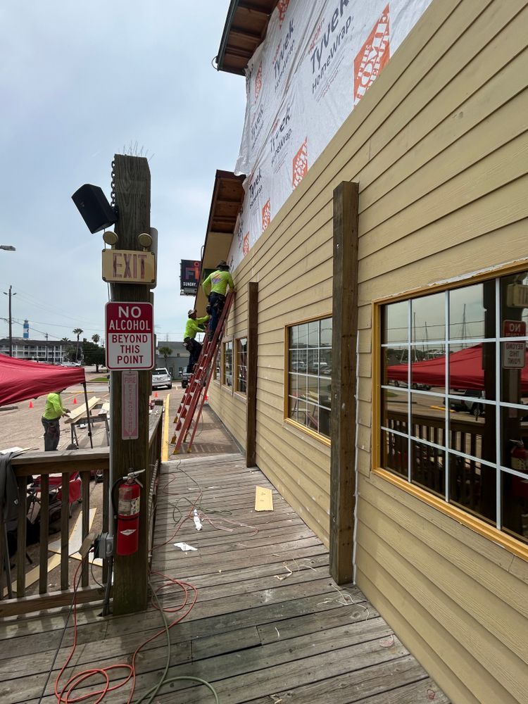 Workers installing siding on a building exterior; brown siding, windows, and red ladder.